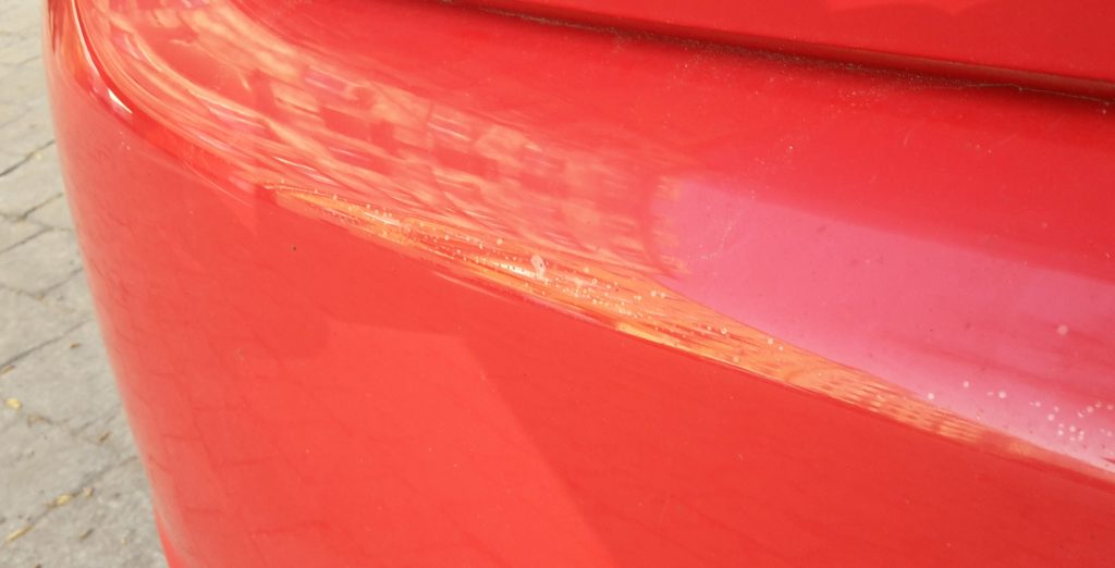 Multiple clear coat blisters on a red, plastic bumper.