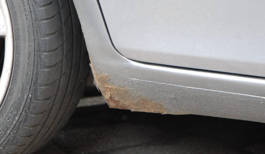 A large patch of corrosion on a side sill of a used, grey car.